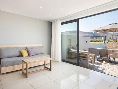 Moderne woonkamer met grijze bank en toegang tot een terras met zithoek en parasol.