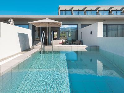 Modern zwembad voor een wit hotelgebouw met ligstoelen en parasol.