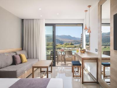 Helles Hotelzimmer mit Sofa, Tischen und Balkon mit Bergblick.