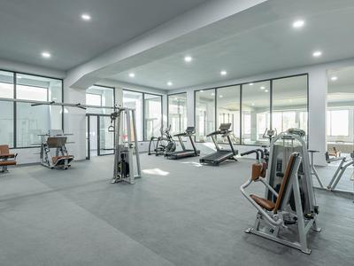 Moderner Fitnessraum mit Trainingsgeräten und großen Fenstern für viel Tageslicht.