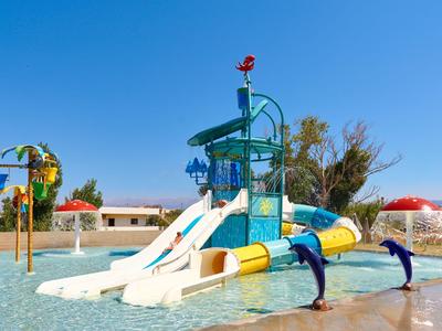 Bunter Wasserspielplatz mit Rutschen und Delphinskulpturen in einem Hotelpool unter blauem Himmel.
