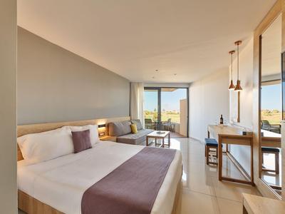 Modernes Hotelzimmer mit großem Bett, Schreibtisch, Stühlen und Panoramablick auf die Natur.