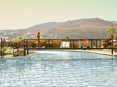 Ein Swimmingpool mit Brücke und Bergen im Hintergrund bei sonnigem Wetter.