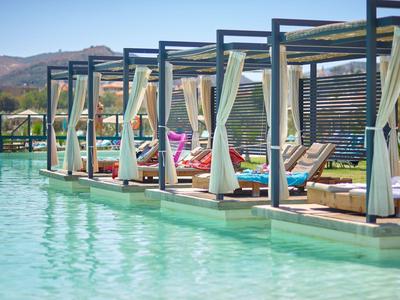 Luxuriöse Poolbetten mit weißen Vorhängen und blauem Wasser in einer sonnigen Resort-Umgebung.