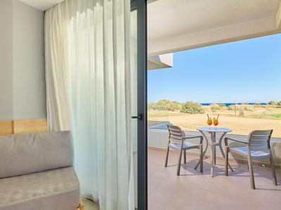 Balkon mit zwei Stühlen und Tisch mit Getränken, Aussicht auf Meer und Sanddünen, angrenzend an ein Zimmer.