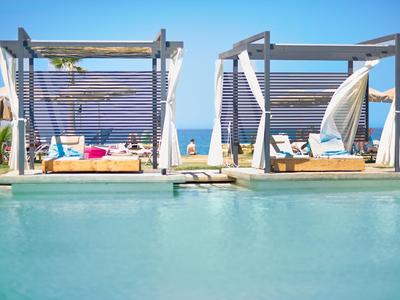 Moderne, offene Poolliegen unter Holzpavillons mit Blick auf das Meer an einem sonnigen Tag.