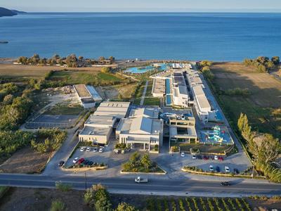 Luftaufnahme eines Hotelresorts am Meer mit Pools, Gebäuden und Parkplätzen.
