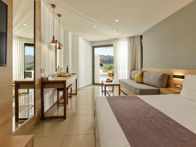 Helles Hotelzimmer mit Bett, Sofa, Schreibtisch und Blick auf Balkon mit Bergblick.