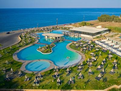 Großer Hotelpool mit Liegestühlen, Sonnenschirmen und Meer im Hintergrund an einem sonnigen Tag.