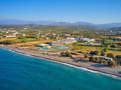 Küste mit klarem blauen Wasser, Sandstrand und Ferienanlage mit Pools und Gebäuden im grünen Tal.