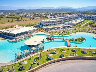 Großes Hotelresort mit mehreren Pools, Liegestühlen, Palmen und Bergen im Hintergrund.