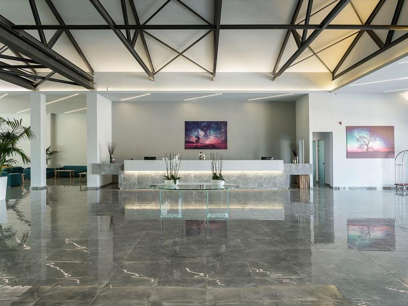 Moderne hotel lobby met marmeren vloer, receptiebalie en decoratieve planten onder zichtbare plafondbalken