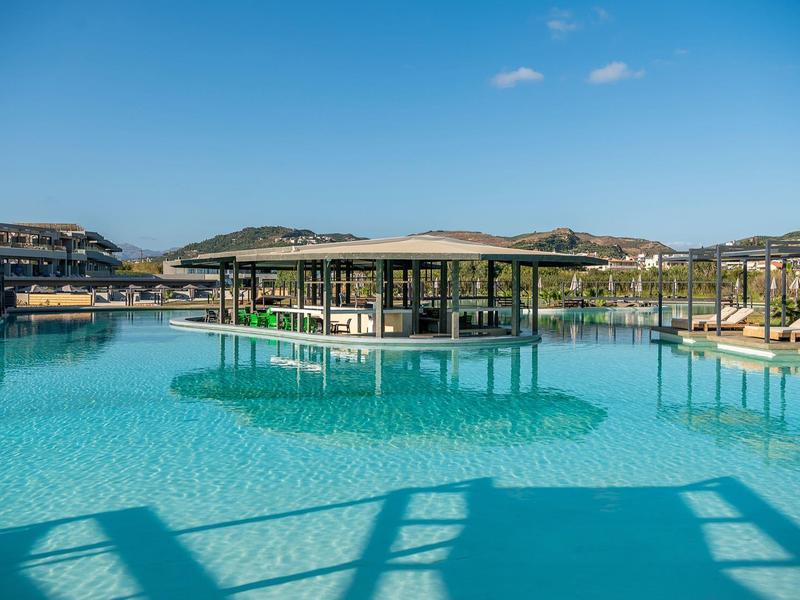 Groot zwembad met geïntegreerde swim-up bar en parasols bij een hotelresort onder een heldere hemel.