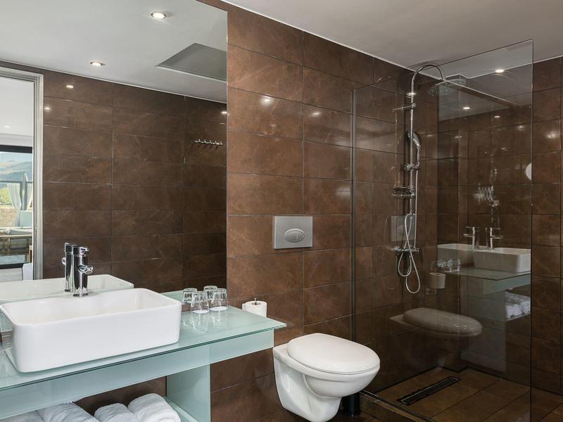 Moderne badkamer met bruine tegels, witte toilet, wastafel en glazen douchecabine.