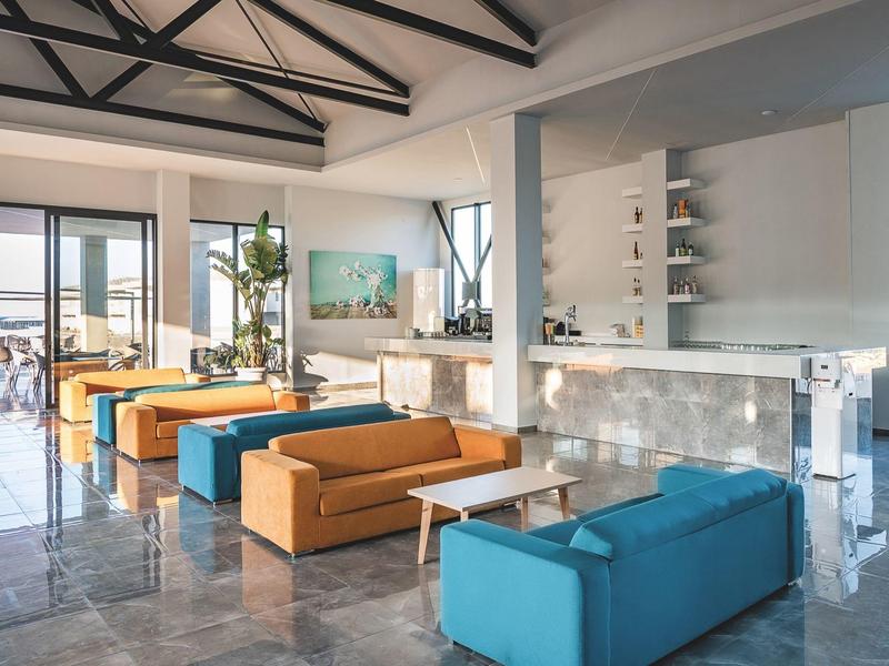 Moderne hotellounge met kleurrijke banken, glazen tafels en een bar met planken.