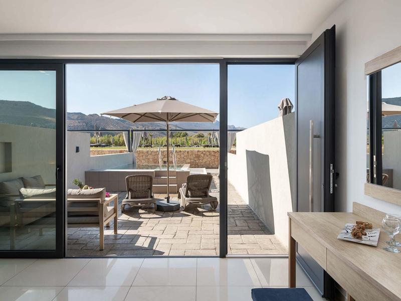 Heldere hotelterras met zitgedeelte en parasol tegen bergachtergrond.