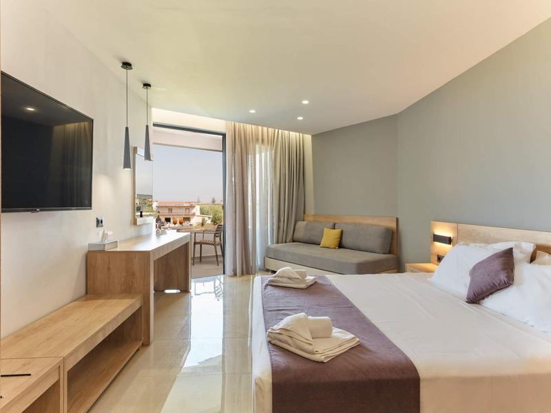 Moderne hotelkamer met tweepersoonsbed, loungegedeelte en balkon met zeezicht.