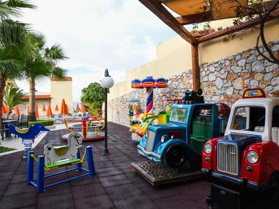 Children's playground with colorful mini cars and carousel in a hotel outdoor area during daylight.