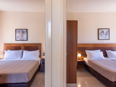 Zwei nebeneinanderliegende Hotelzimmer mit großen Betten, Nachttischen und Wandbildern.