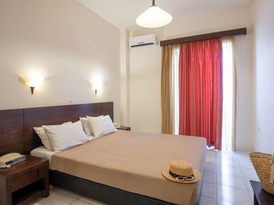 Bright hotel room with double bed, nightstands, air conditioning, and red curtains on the window.