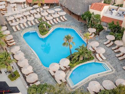 View of a hotel pool area with lounge chairs and umbrellas in a Mediterranean setting.