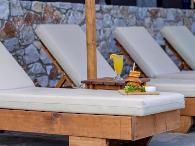 Holzliegen mit weißen Polstern neben einer Steinmauer, auf einer Liege ein Burger und ein Getränk.