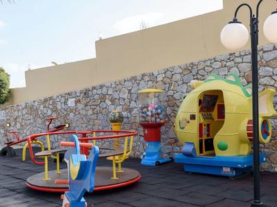 Colorful carousel and play equipment in a paved yard in front of a stone wall.