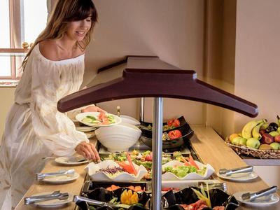 Woman serves salad at a buffet with fruits and vegetables in a bright room.