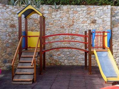 Kinderspielplatz mit Rutsche, Brücke und Treppe vor einer Steinmauer
