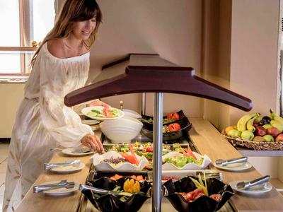 Frau im weißen Kleid bedient sich am Buffet mit verschiedenen Obst- und Salatschalen.