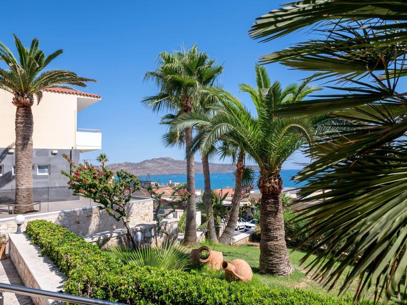 Tropical garden area with palm trees and sea view next to a white building.
