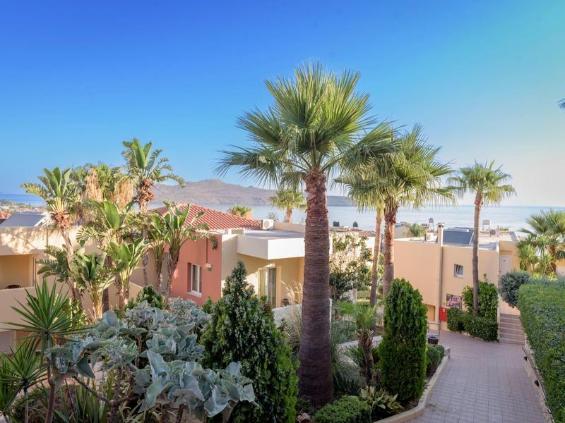 Pathway surrounded by buildings, palm trees, and blooming plants under a blue sky.