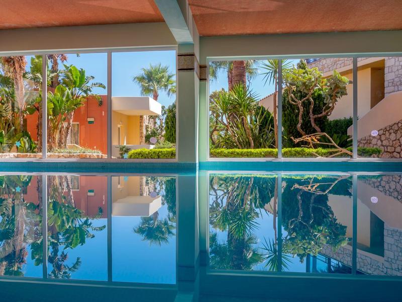 Indoor pool with large windows overlooking tropical plants and vacation houses.