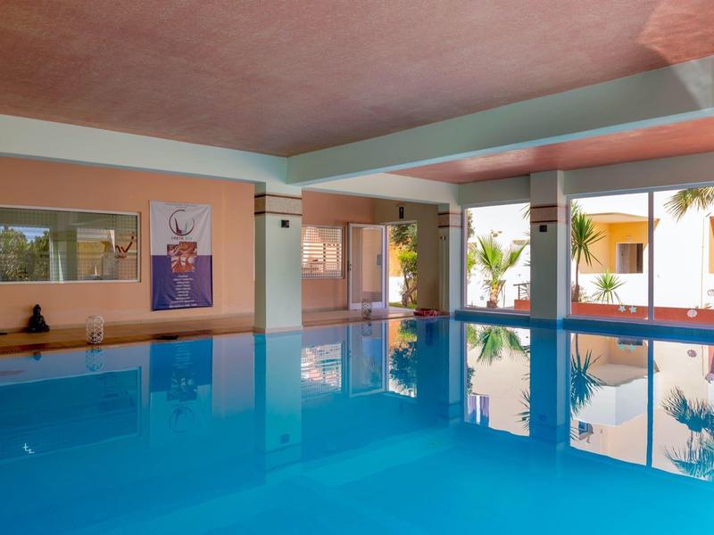 Indoor pool with large windows overlooking a courtyard with palm trees and orange walls.