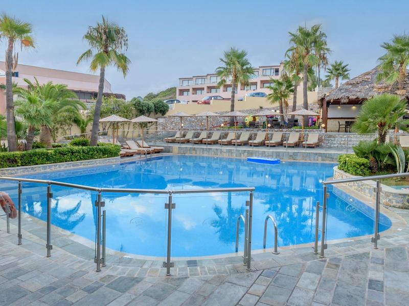 Large pool with glass railing and sun loungers at tropical hotel resort.