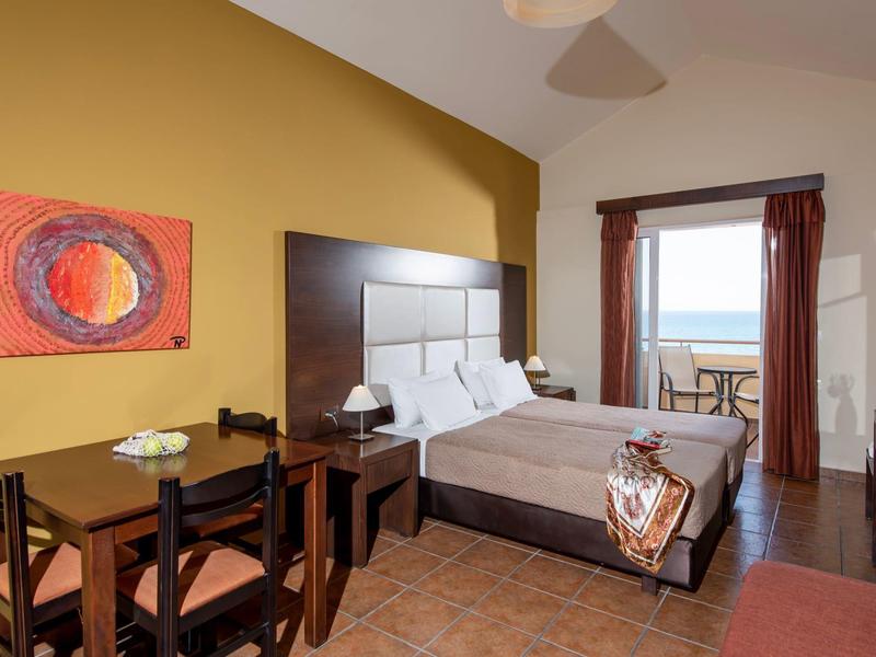 Hotel room with double bed, dark wood furniture, and balcony overlooking the sea.