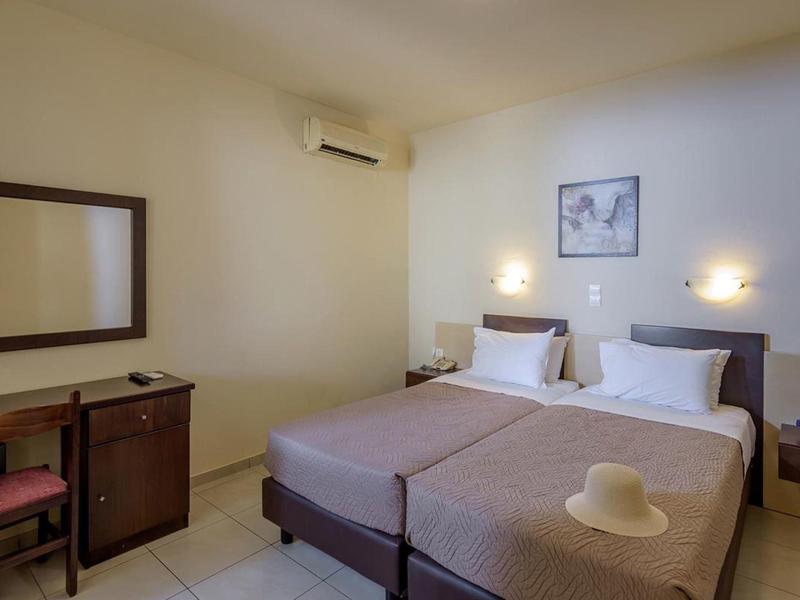 Bright hotel room with two single beds, a desk with chair, and a wall mirror.