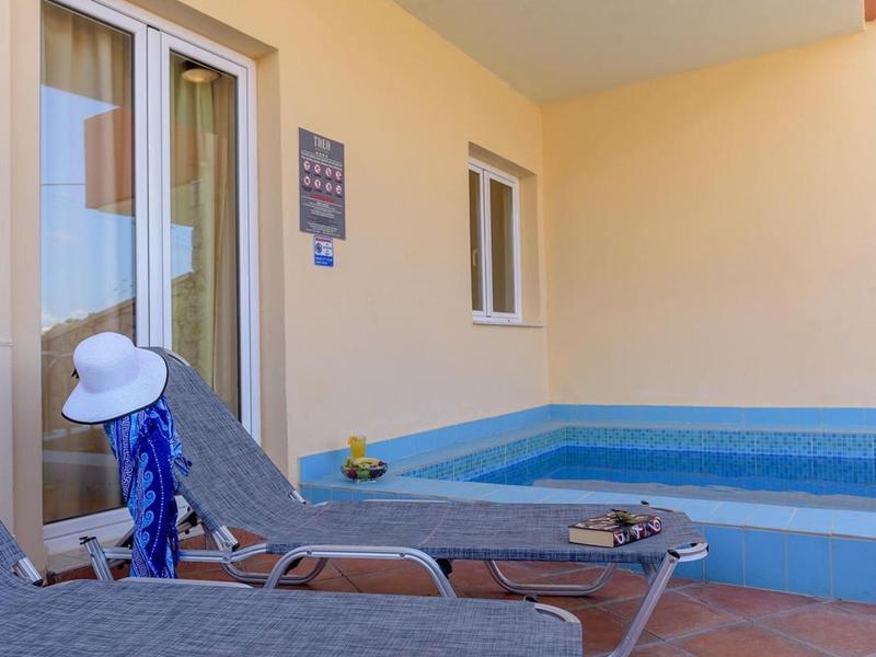 Two lounge chairs next to a small pool on a terrace with beige wall.