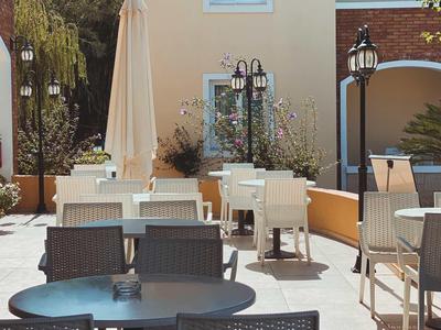 Zonnig terras met tafels, stoelen en grote parasols bij een hotel.