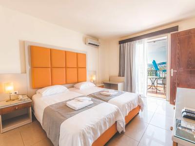 Lichte hotelkamer met twee eenpersoonsbedden, oranje hoofdeinde en balkon met zeezicht.