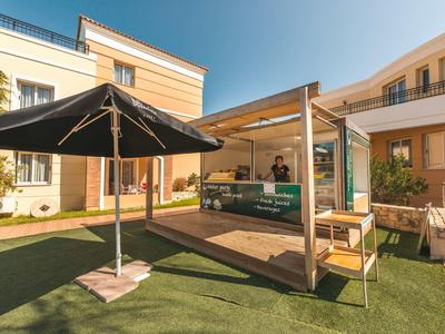Moderne buitenkraam met parasol en zitgelegenheid voor een hotelgebouw tijdens zonnig weer
