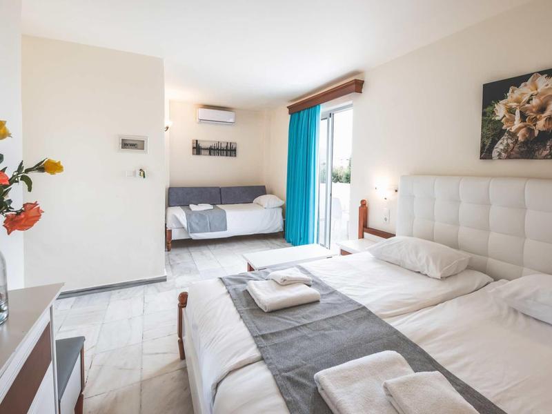 Lichte hotelkamer met twee eenpersoonsbedden, bank, bloemen en blauwe gordijnen.