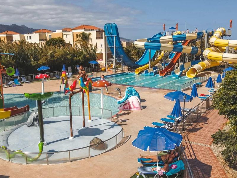 Waterpark met meerdere glijbanen, kinderbad en blauwe parasols.