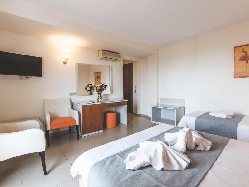 Lichte hotelkamer met twee bedden, tv, zithoek en bureau.