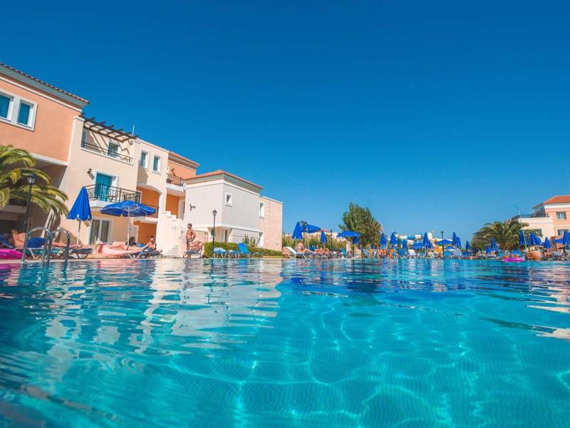 Duidelijk zwembadzicht bij hotel met parasols en gebouwen onder heldere lucht