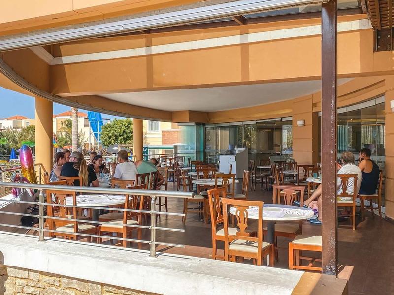 Overdekt restaurantterras met tafels, stoelen en gasten bij daglicht.