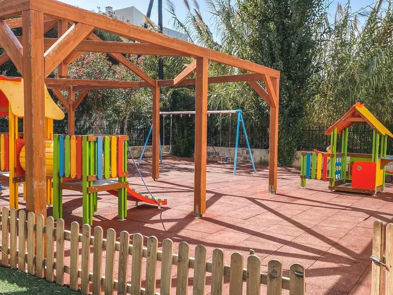 Kleurrijke speeltuin met schommels en klimtoestellen omgeven door een hek.