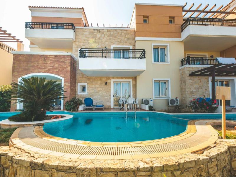 Modern hotelcomplex met zwembad, omgeven door stenen muren en balkons met uitzicht op het water.