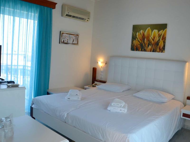 Licht hotelkamer met tweepersoonsbed, twee handdoeken en blauwe gordijn bij het raam.