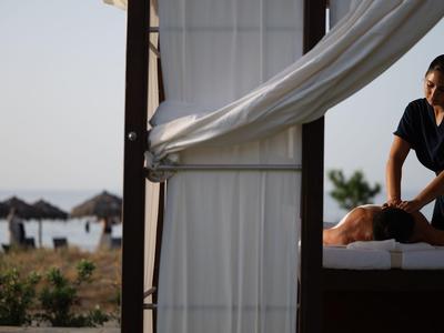 Femme recevant un massage dans un pavillon de plage avec un rideau flottant et vue sur la mer.